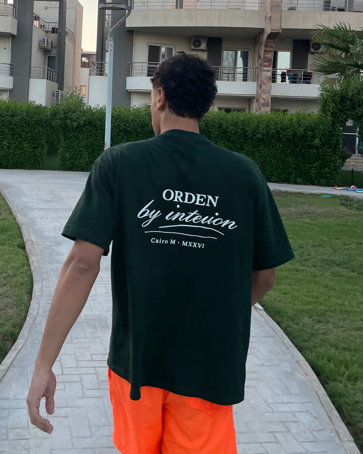 By Intention Tee in Green — worn back view, oversized fit with ORDEN back print, outdoors at dusk on the North Coast